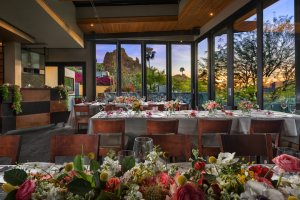 Praying Monk dining room decorated with spring florals with sun setting behind Camelback Mountain in background.