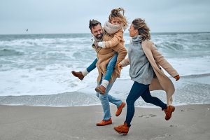 Family of three walking on the beach in winter clothing