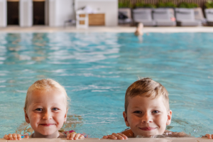 Two children smile at the edge of an indoor pool