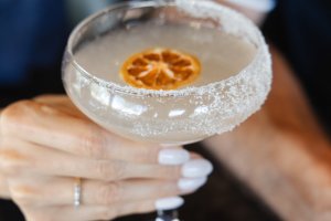Close up of woman holding cocktail in fine glassware with citrus garnish and sugar-lined rim.