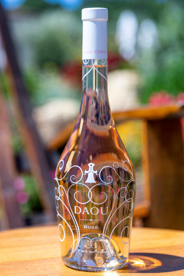 A bottle of Daou rose wine sits on a wooden table with greenery in the background.