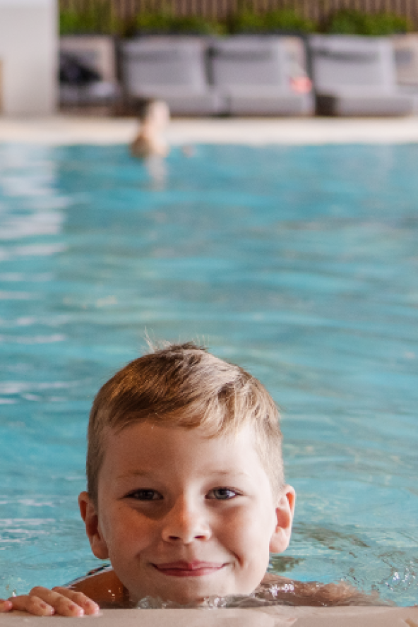 Two children smile at the edge of an indoor pool