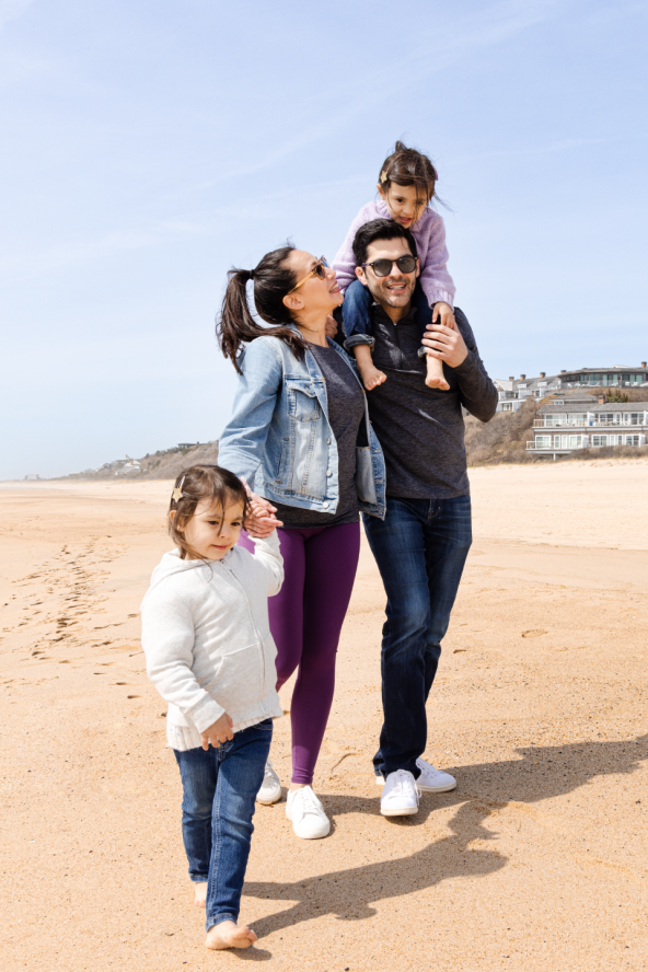 Husband and wife walking along beach and laughing with two daughters.