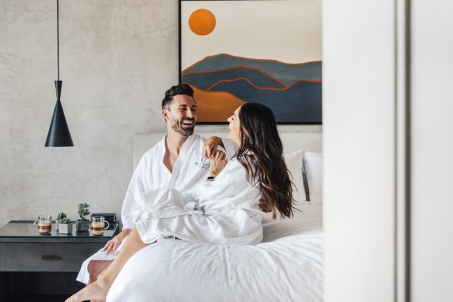 Couple in spa robes laughing and enjoying morning coffee on bed of casita.