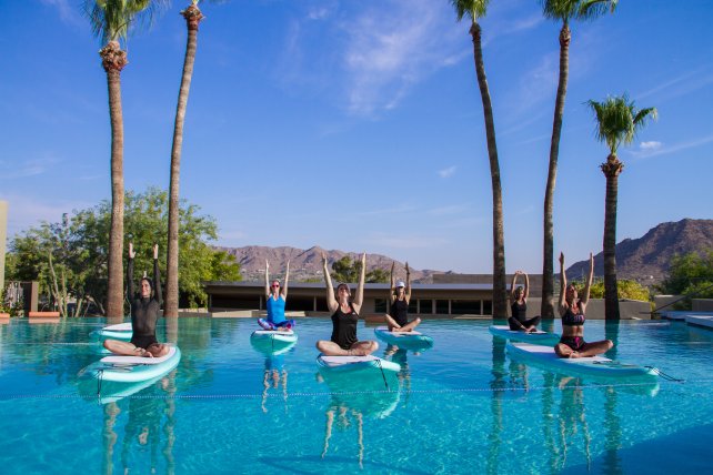 A group of people balancing on paddleboards in a pool.