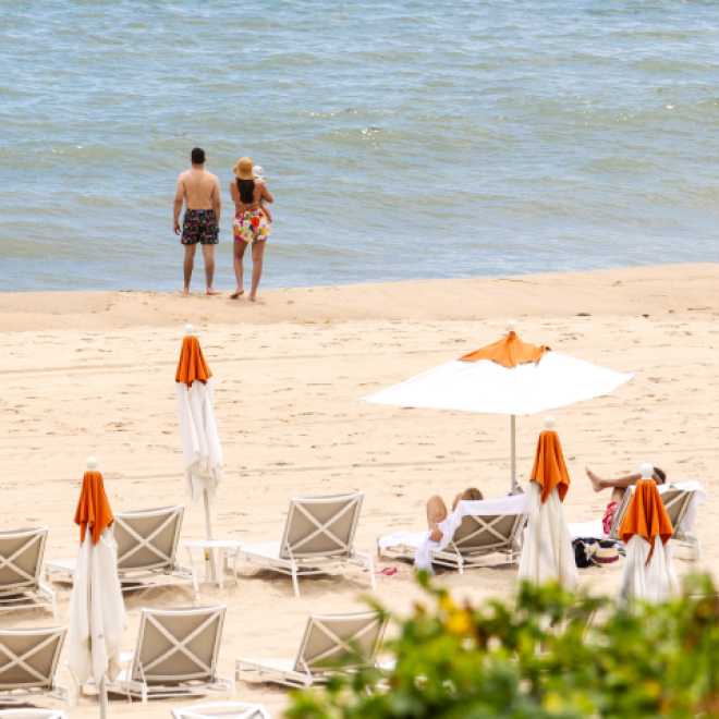 A couple with a small child stand near the water's edge on the private beach at Gurney's Montauk