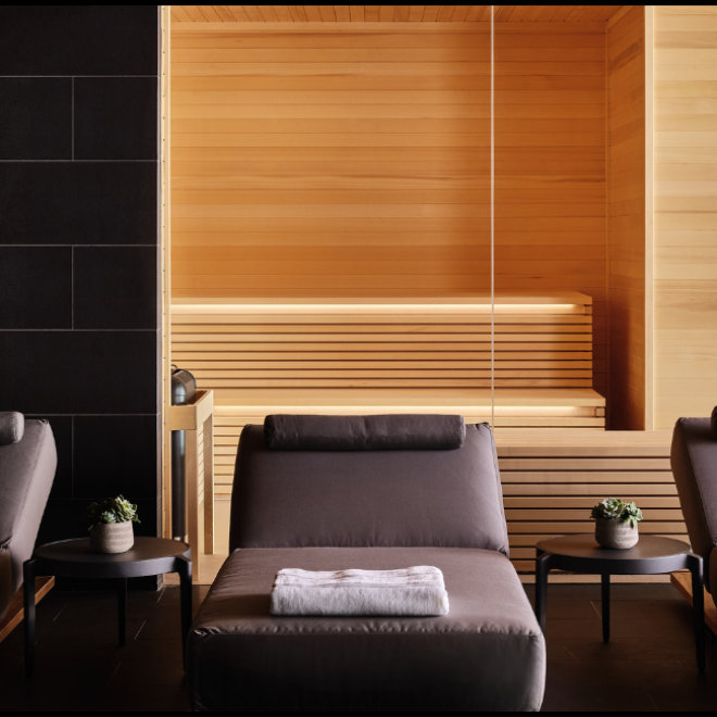 Three gray lounge chairs lined up with the sauna in the background at the Seawater Spa BathHouse