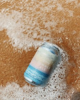 a can of Gurney's Summer Ale in the sand and some waves