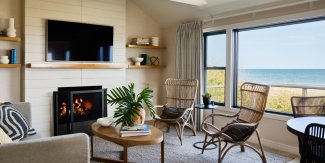 Cozy beachside living room with a fireplace, wicker chairs, a sofa, and a large window overlooking the ocean.