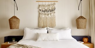 Cozy bedroom with a large bed, white linens, woven wall hanging, and wicker pendant lights, creating a warm, inviting atmosphere.