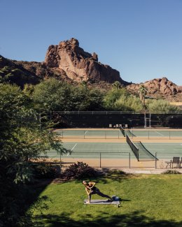 Woman doing yoga on grass in front of tennis courts with view of Praying Monk in the background.